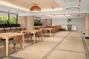 Un espace de restauration moderne avec des tables et des chaises en bois, un grand luminaire suspendu et une vue sur la verdure environnante.