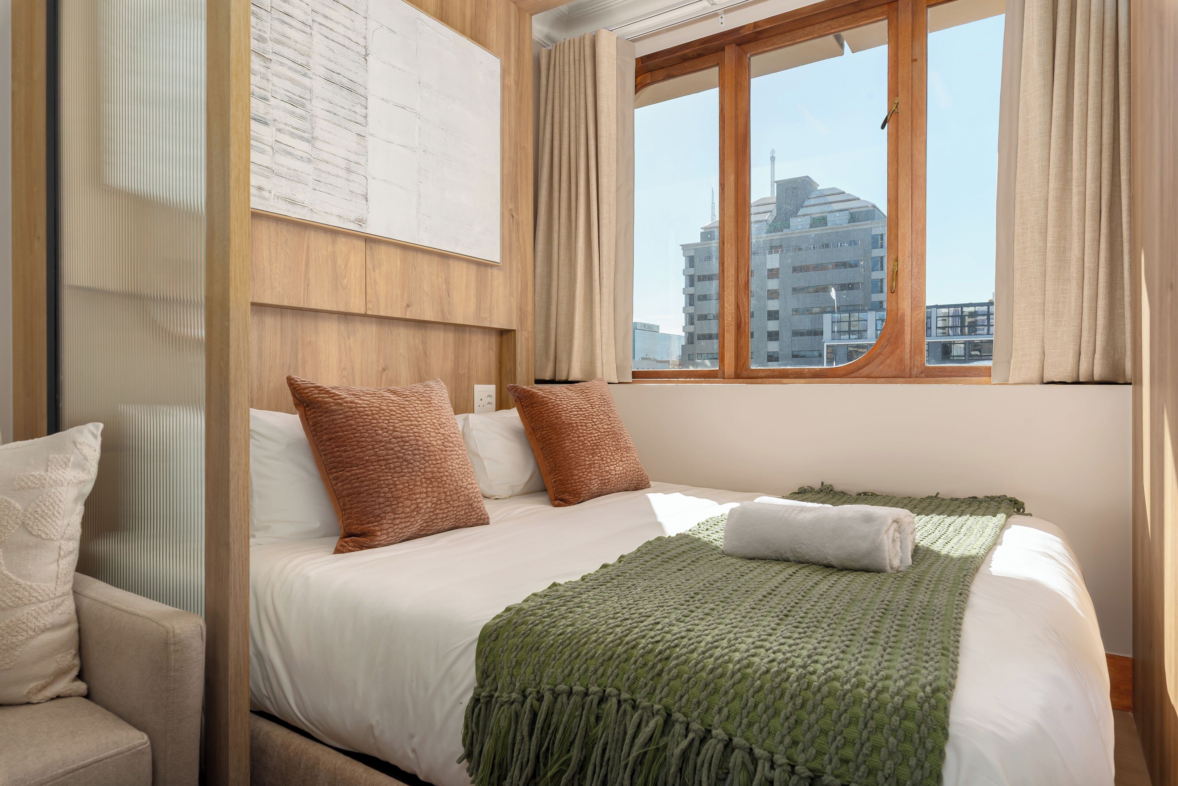 A hotel room with a bed, a view of buildings, and a window with curtains.
