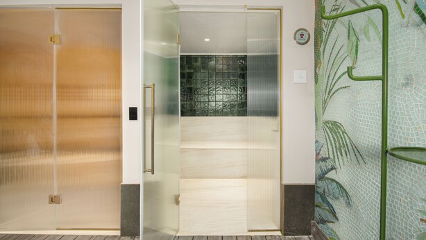 Habitación de hotel con puerta corredera, zona de ducha con azulejos y barandilla de metal verde.