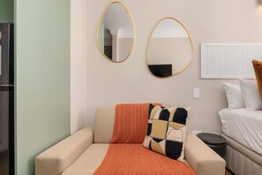 Ein Zimmer mit einer Couch, einer Decke, zwei Wandspiegeln, einem Heizkörper und einem Bett mit Kissen.