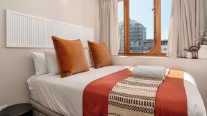 Habitación de hotel con una cama grande, una ventana con cortinas, un radiador y vistas a la ciudad.