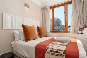 A hotel room with a large bed, a window with curtains, a radiator, and a view of the cityscape. - Charlie and the Chairman | Designer CBD Apartment (Cape Town)