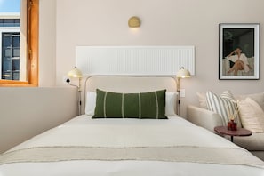 A bedroom with a bed, bedside lamps, a radiator, a framed picture, and a window. - Charlie and the Chairman | Modern CBD Studio (Cape Town)