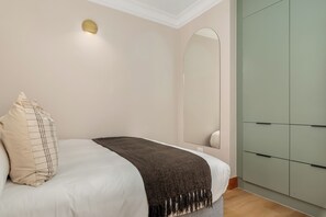 A bedroom with a bed, a bedside lamp, a wardrobe, and a mirror. - Charlie and the Chairman | Modern CBD Apartment (Cape Town)