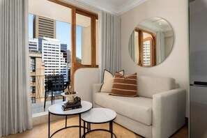 A modern living room with a sofa, a round mirror, a small table with books, and a view of the cityscape through large windows. - Charlie and the Chairman | Modern CBD Apartment (Cape Town)