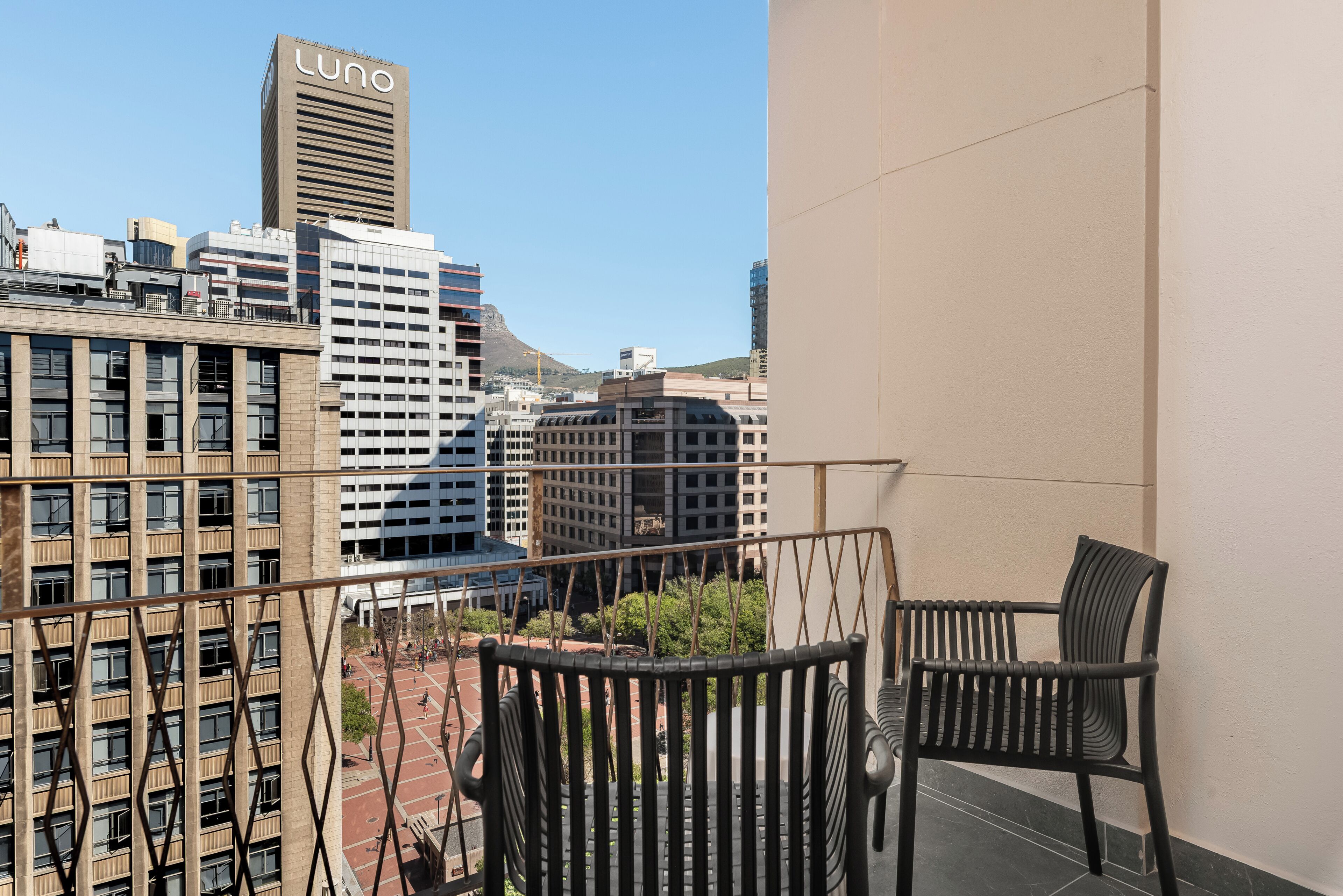 A balcony with two chairs, overlooking a cityscape with various buildings, including one with 'Luno' signage.