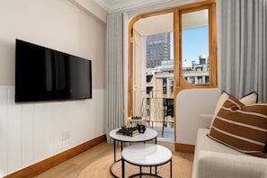 A modern living room with a flat-screen TV mounted on the wall, a small round table with books and a candle, and a sofa with decorative pillows. - Charlie and the Chairman | Modern CBD Apartment (Cape Town)