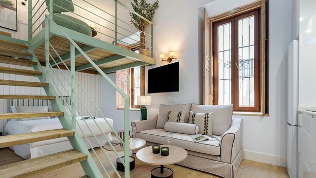 Un salon moderne avec un escalier, un ensemble de canapés, une table basse et un téléviseur.