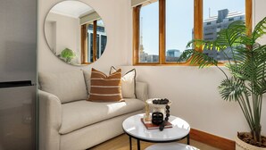 A modern living room with a sofa, a round mirror, a coffee table, and a view of the city through large windows. - Charlie and the Chairman | Contemporary Stay (Cape Town)