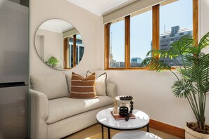 Ein modernes Wohnzimmer mit einer Couch, einem runden Spiegel, einem Couchtisch und Blick auf die Stadt durch große Fenster.