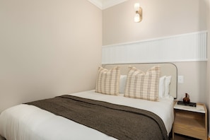 A hotel room with a bed, a nightstand, a lamp, and a wall-mounted light fixture. - Charlie and the Chairman | Contemporary Stay (Cape Town)