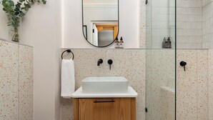 A bathroom with a white sink, wooden cabinet, and a glass shower enclosure. - Charlie and the Chairman | Contemporary Stay (Cape Town)
