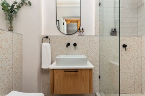 Ein Badezimmer mit weißem Waschbecken, Holzschrank und Duschkabine aus Glas.