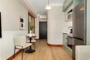 A modern kitchen with a built-in oven and refrigerator, a dining area with a table and chairs, and a hallway leading to a dark door. - Charlie and the Chairman | Contemporary Stay (Cape Town)