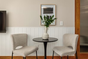 Ein Zimmer mit zwei Stühlen, einem Tisch, einer Topfpflanze und einem gerahmten Bild an der Wand.