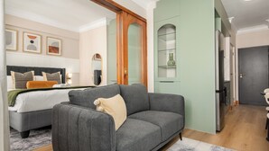 Quarto de hotel moderno com um sofá cinzento, uma cama com colcha branca, um guarda-roupa de madeira e uma parede verde.