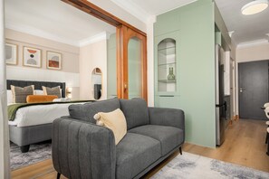 A modern hotel room with a grey sofa, a bed with a white duvet, a wooden wardrobe, and a green wall. - Charlie and the Chairman | Designer Escape (Cape Town)