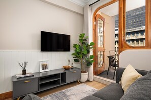 A modern living room with a flat-screen TV mounted on the wall, a grey entertainment unit, a large potted plant, and a view of a building through an open door. - Charlie and the Chairman | Designer Escape (Cape Town)