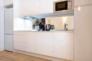 A modern kitchen with white cabinetry, a built-in microwave, a coffee machine, and a sink with a faucet. - Genteel Home Antonio Marchena 002 (Seville)