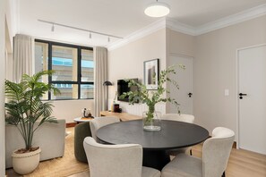 Un coin repas moderne avec une table ronde, six chaises, une plante en pot et une fenêtre avec des rideaux.