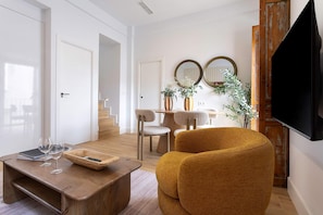 A modern living room with a wooden coffee table, a sofa, a dining table with chairs, and a flat-screen TV mounted on the wall. - Genteel Home Antonio Marchena 202 (Seville)