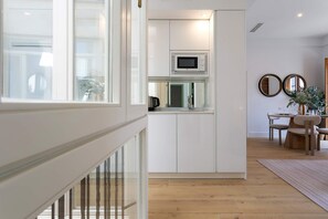 A modern kitchen with white cabinetry, a built-in microwave, and a view of the dining area with a wooden table and chairs. - Genteel Home Antonio Marchena 202 (Seville)