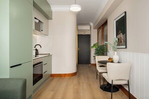 Un couloir étroit, avec une cuisine d’un côté, un coin repas avec une table et des chaises, et une porte donnant sur une autre pièce.
