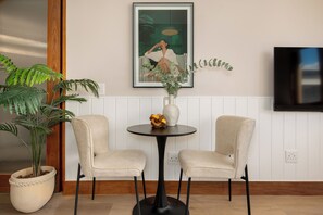 A room with two chairs, a table, a potted plant, a framed artwork, and a television on the wall. - Charlie and the Chairman | Elevated City Stay (Cape Town)