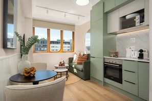 A modern kitchen with green cabinets, a Bosch oven, and a view of buildings through large windows. - Charlie and the Chairman | Elevated City Stay (Cape Town)