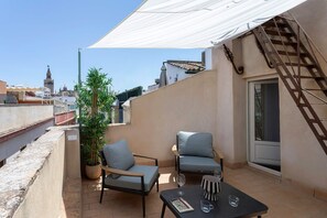 Una terraza en la azotea con dos sillas, una mesa y una planta en maceta.