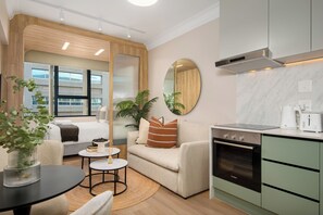 A modern hotel room with a kitchenette, a sofa, a dining table, and a large window. - Charlie and the Chairman | Modern CBD Apartment (Cape Town)