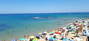 Una platja amb aigua turquesa cristal·lina, gent nedant i nombrosos paraigües de colors.
