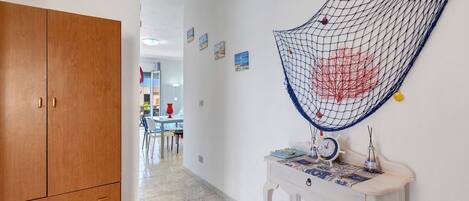 A hallway with a wooden wardrobe, a white wall with a decorative net, and a small table with a clock and decorative items.