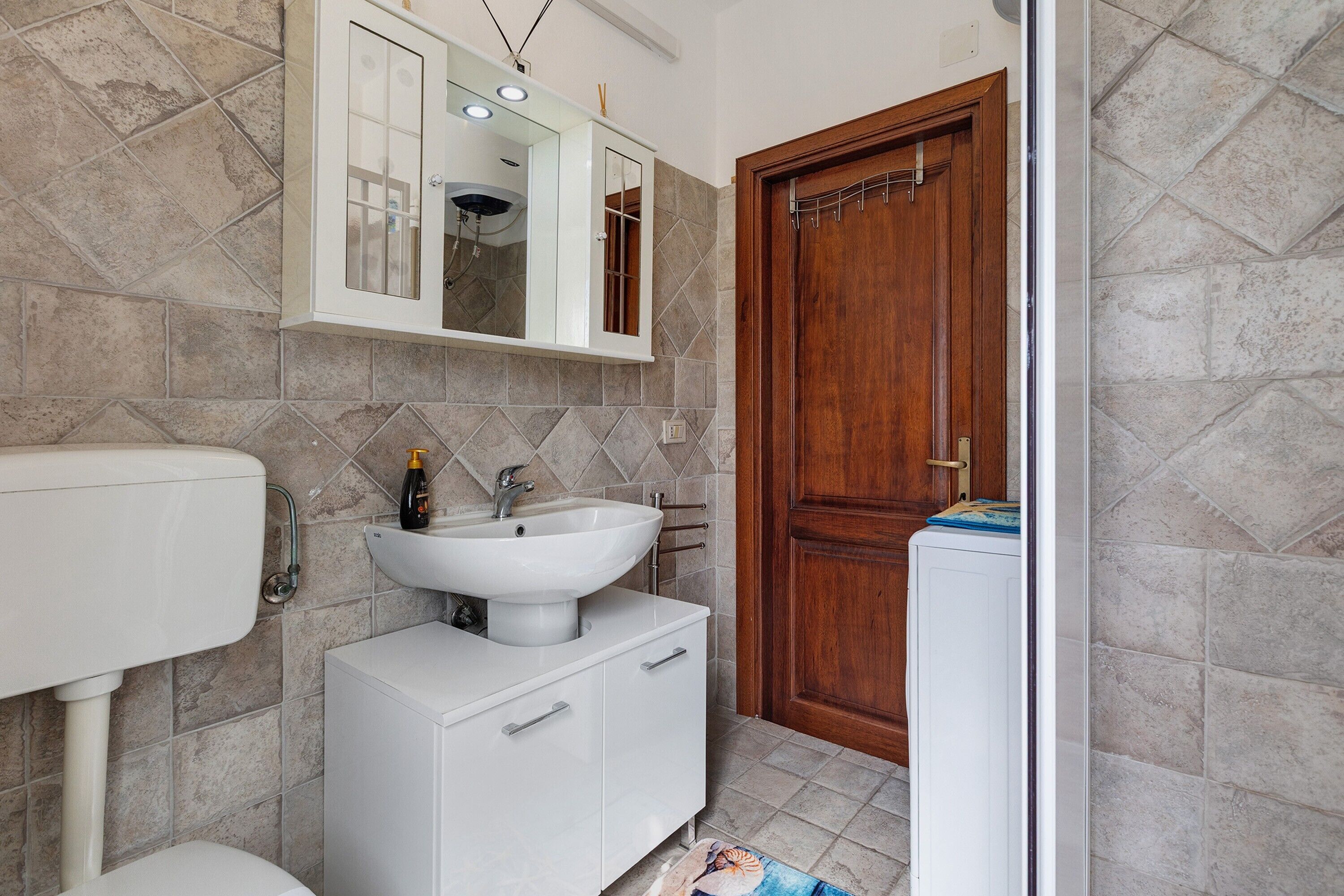 Un bagno con un lavandino bianco, uno specchio, un water e una porta in legno.