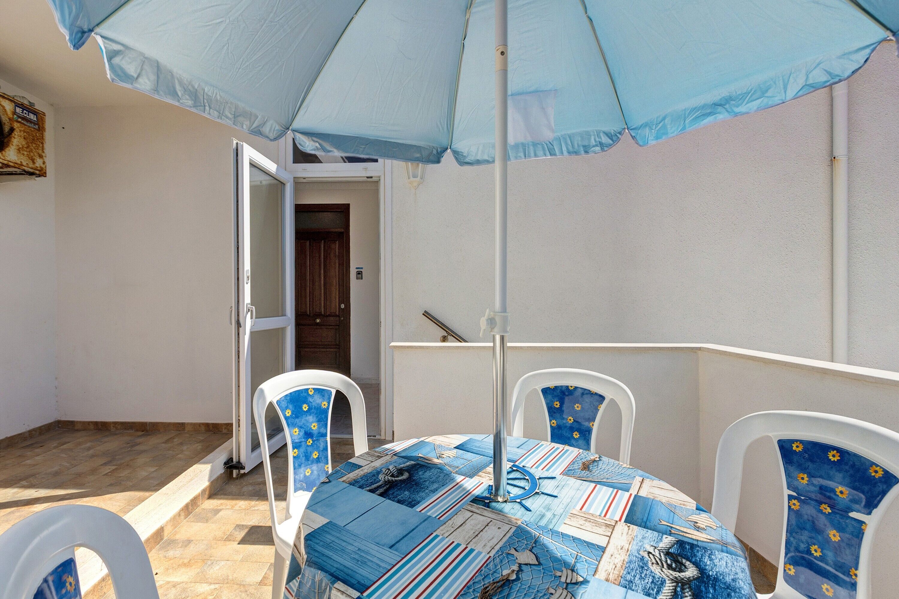 Une terrasse avec une table et des chaises, un parasol et une porte donnant sur un espace intérieur.
