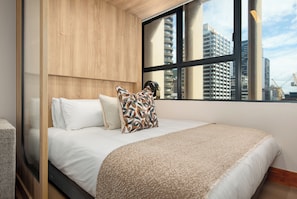 A hotel room with a large bed, a window with a view of buildings, and a wooden headboard. - Charlie and the Chairman | Sleek Studio Stay (Cape Town)