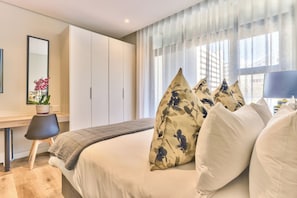 Ein modernes Schlafzimmer mit einem Bett, einem Schreibtisch und einem großen Fenster mit durchsichtigen Vorhängen.