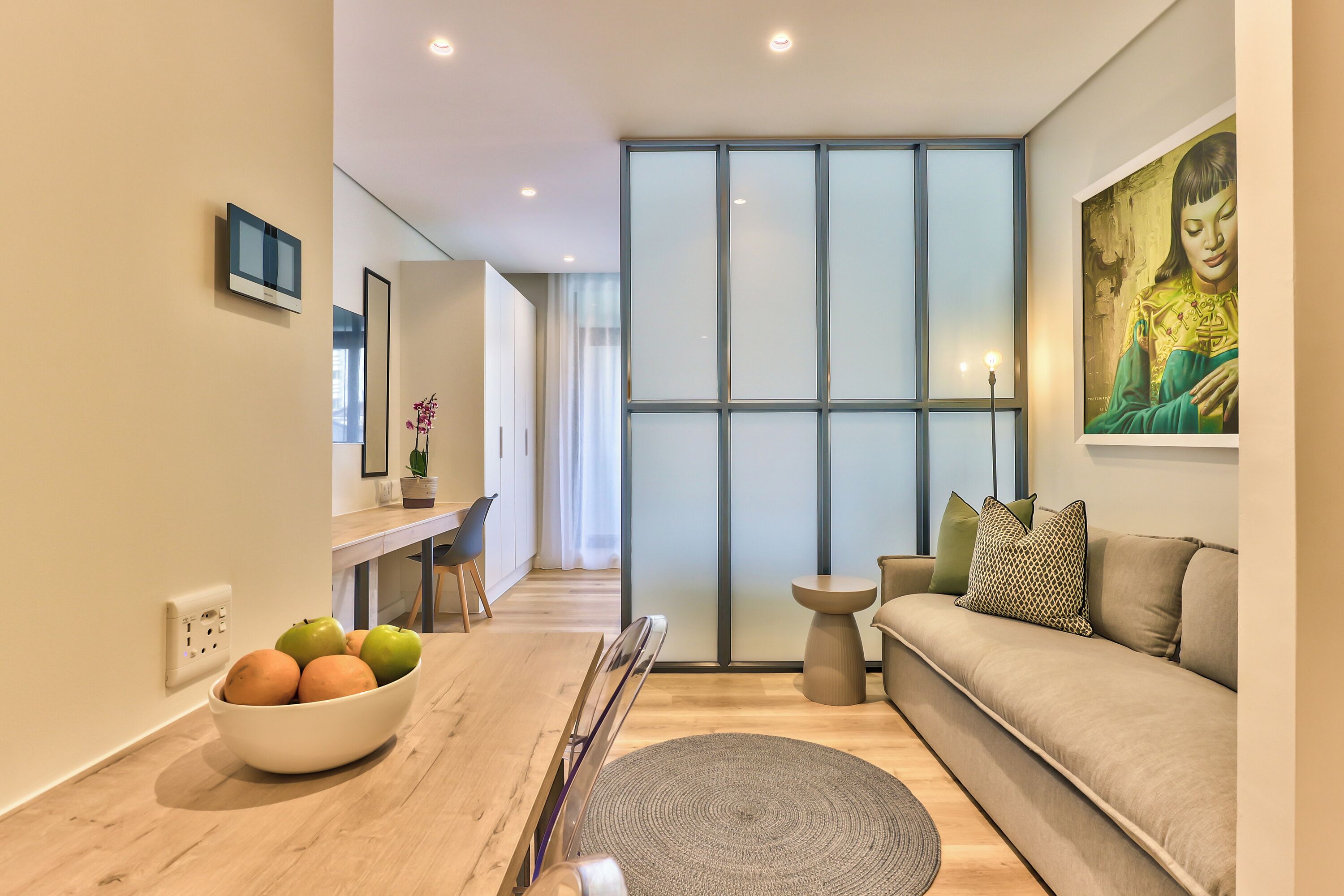 A modern living room with a sofa, a coffee table, a bowl of fruit, and a painting on the wall.