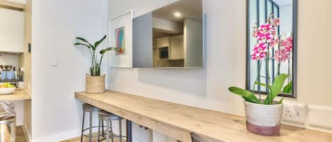 A modern kitchen with a wooden countertop, bar stools, a potted plant, and a large mirror.