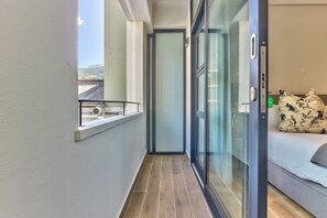 Ein schmaler Gang führt zu einem Schlafzimmer mit Bett, Fenster und Tür.