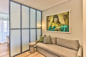 A modern living room with a sofa, a small side table, and a large window with blinds. - The Carrington | Spacious CBD Apartment (Cape Town)