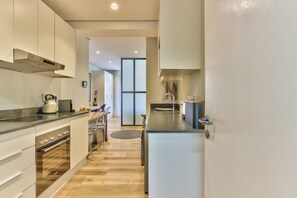 A modern kitchen with stainless steel appliances, a dining area with a round table, and a large window providing natural light. - The Carrington | Spacious CBD Apartment (Cape Town)