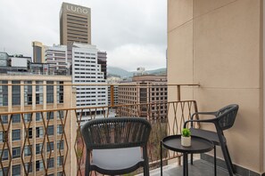 Un balcón con dos sillas y una mesita, con vistas a un paisaje urbano con edificios modernos.