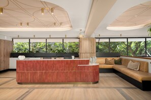 Una zona de recepción moderna con un mostrador de madera, un sofá y grandes ventanales con vistas a zonas verdes.