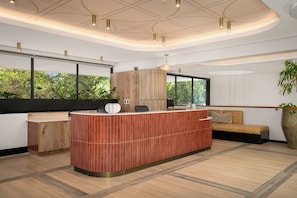 A modern reception area with a wooden reception desk, a sofa, and a large window with a view of greenery. - Charlie and the Chairman |Cityscape Stay and Balcony (Cape Town)