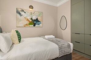 Quarto com cama, almofadas, manta, pintura abstrata pendurada na parede, luminária circular e guarda-roupa.