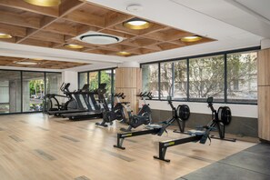 Een sportschool met trainingsapparatuur, grote ramen en een houten plafond.