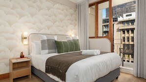Hotellihuone, jossa on suuri sänky, yöpöytä, ikkuna, josta on näkymä rakennuksiin, ja kuviollinen seinä.