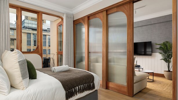Moderni hotellihuone, jossa on suuri sänky, televisio, sohva ja näkymä kaupunkiin.