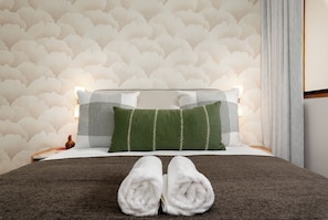 A neatly made bed with two pillows, a brown blanket, and two rolled towels. - Charlie and the Chairman | Modern CBD Apartment (Cape Town)